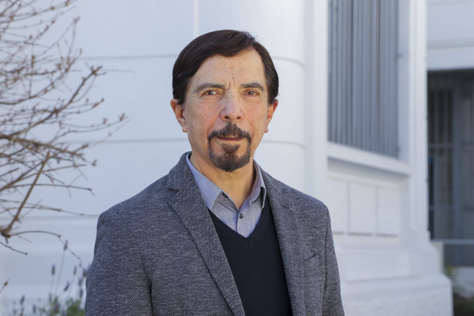 Portrait of a middle-aged man in a gray blazer outdoors, with a modern building in the background.