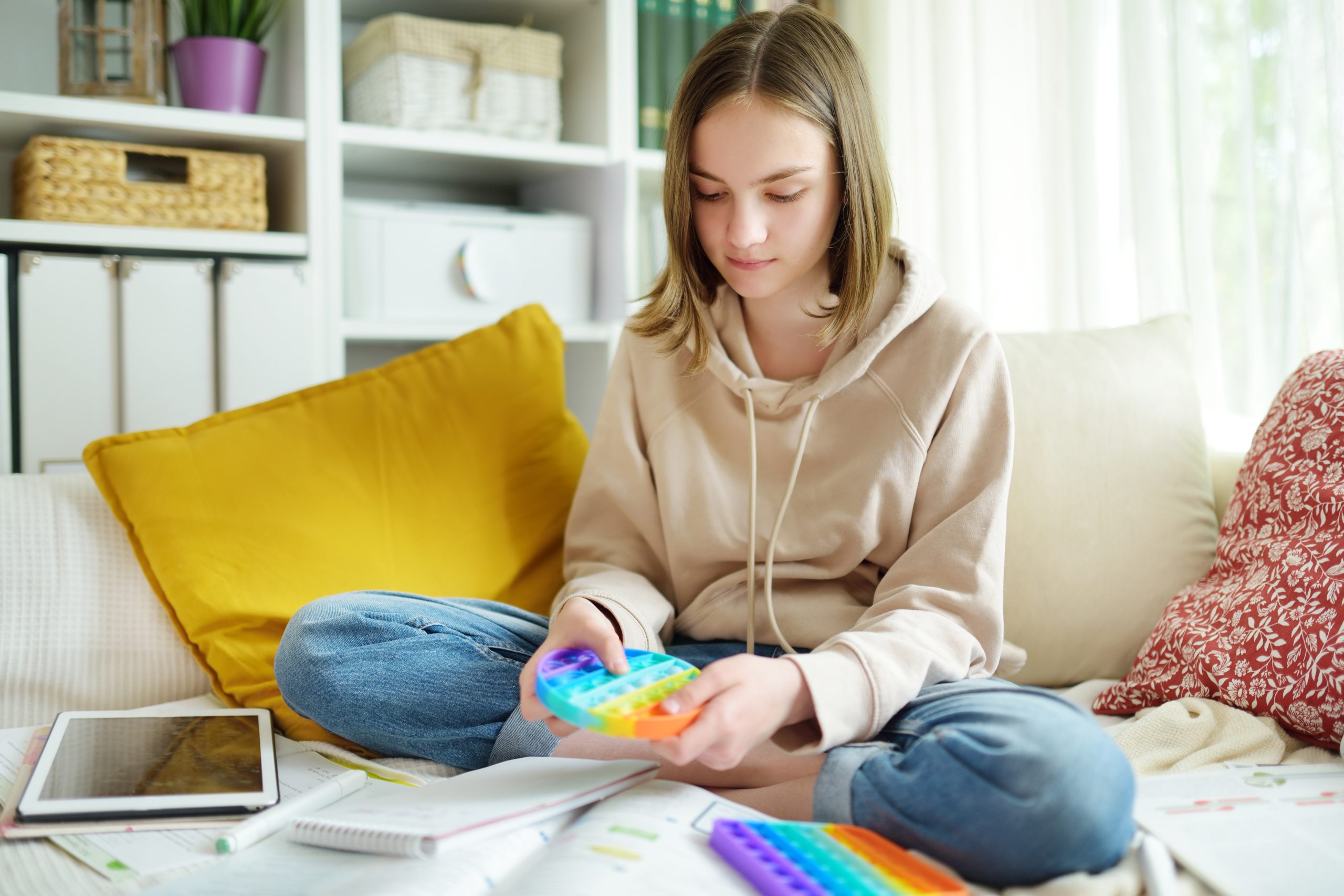 Teenage girl playing with rainbow pop-it fidget toy while studying at home. Teen kid with trendy stress and anxiety relief fidgeting game.