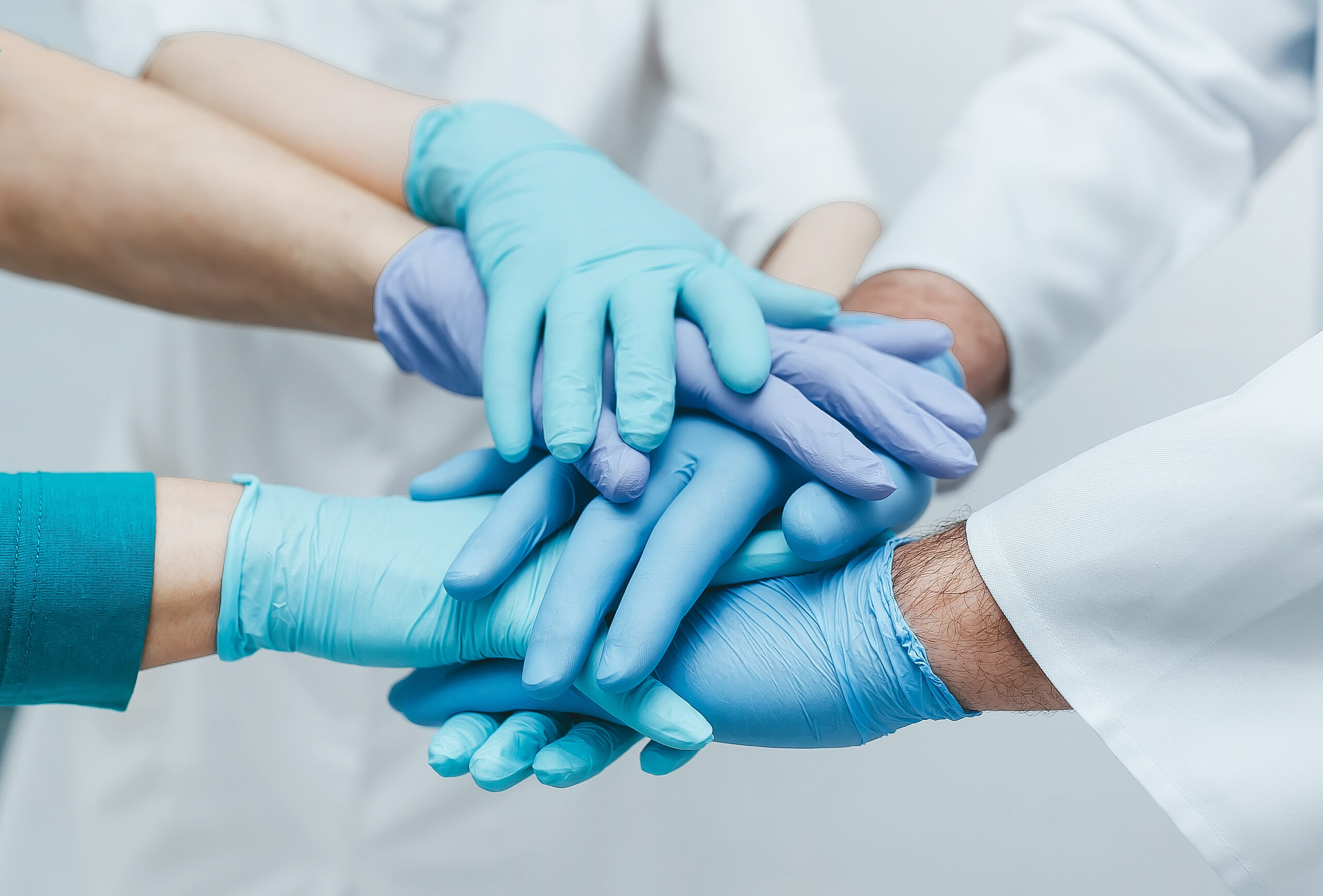 Team of young doctors stacking hands in blue gloves indoor.  med