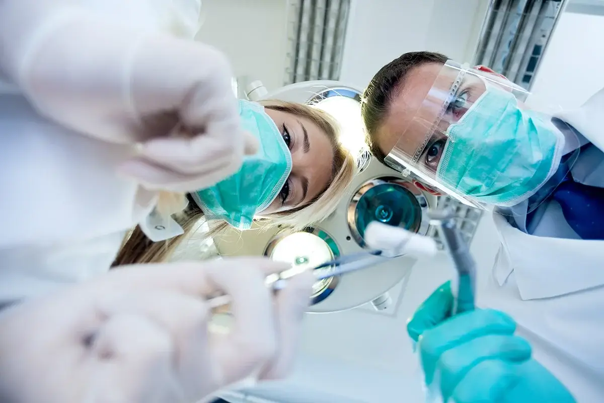 Odontólogos con herramientas realizando tratamiento en silla dental desde la perspectiva del paciente.