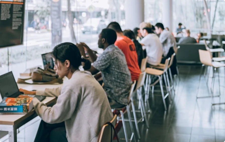 Estudiantes trabajando en una biblioteca, sentados en mesas con libros y computadoras.