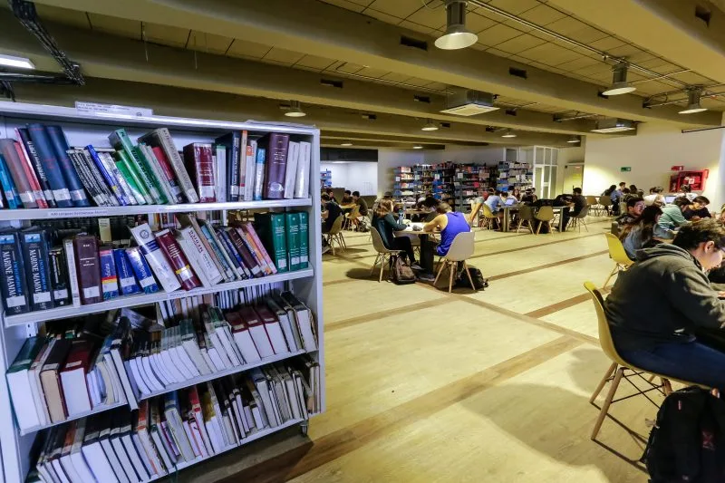 Interior de una biblioteca moderna con estanterías llenas de libros y mesas de estudio.